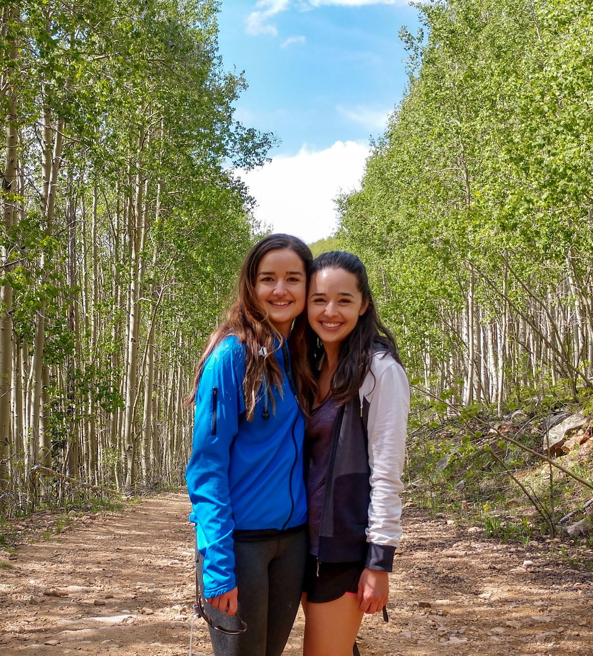 Two girls standing on a trail with aspen trees in the background.
